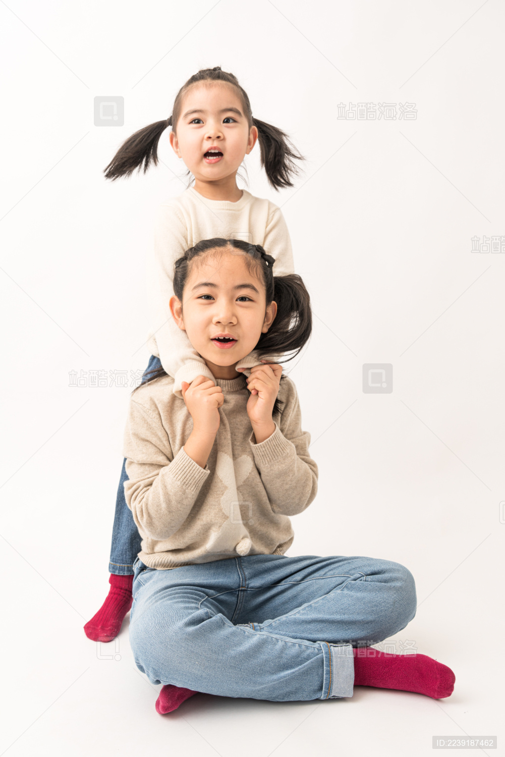 两名坐在白色背景前玩耍的姐妹