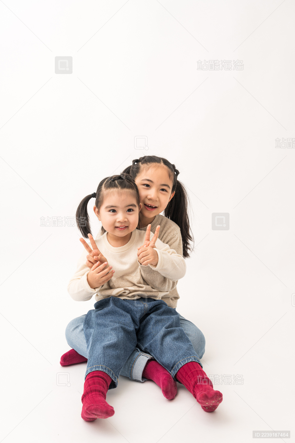 两名坐在白色背景前玩耍的姐妹