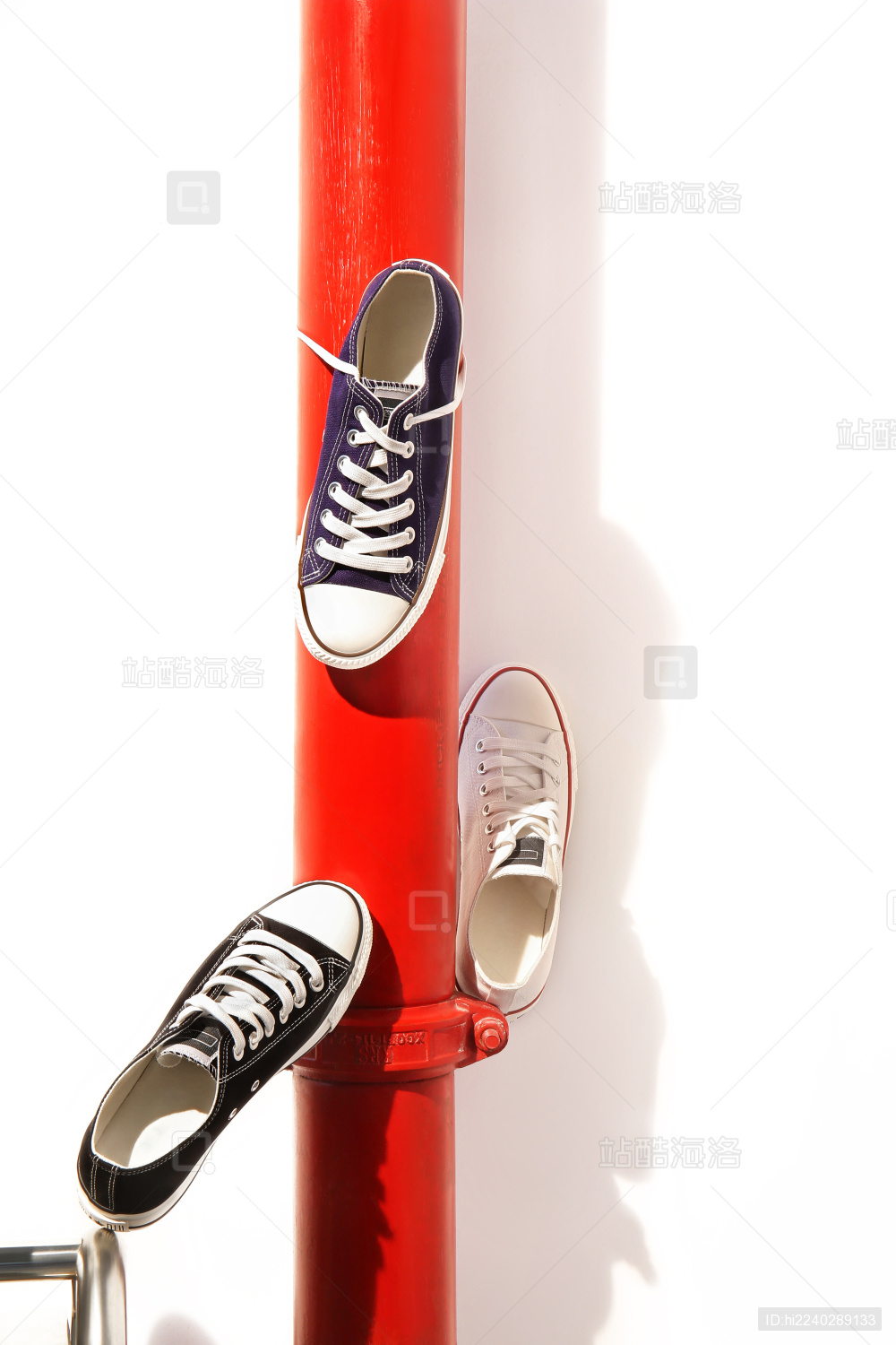 三种不同颜色的帆布鞋斜靠在红色的管道上
