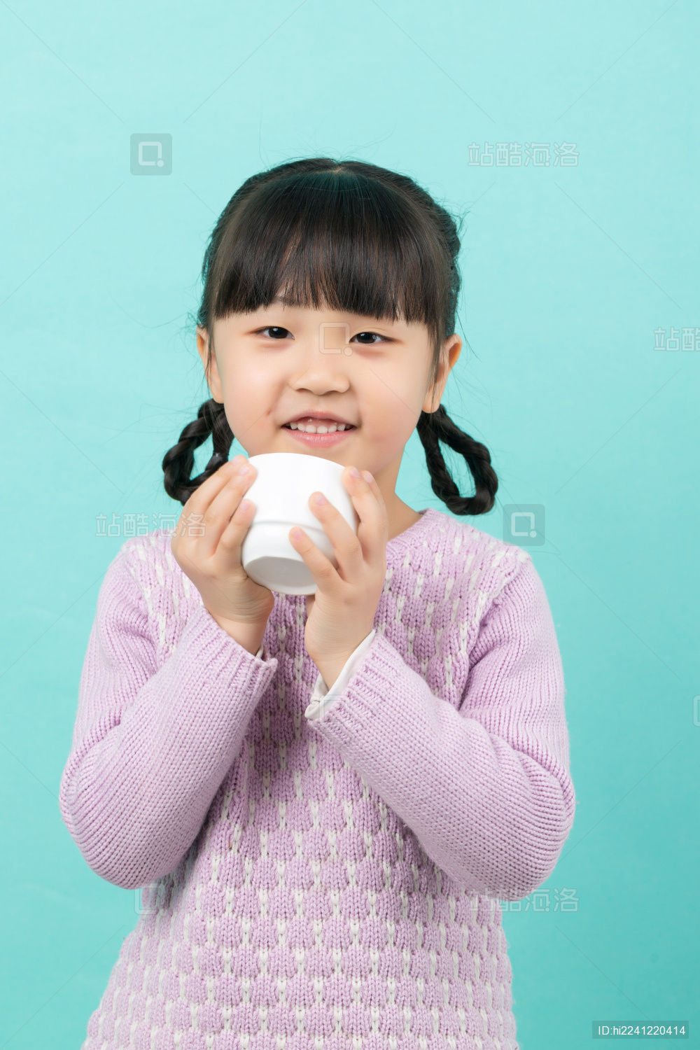 纯色背景前的亚洲小女孩拿着水杯喝水