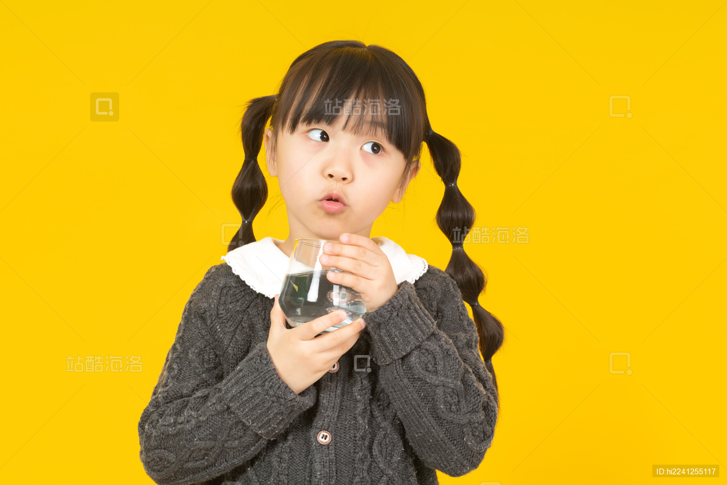 暖黄色背景前拿玻璃杯喝水的中国小女孩