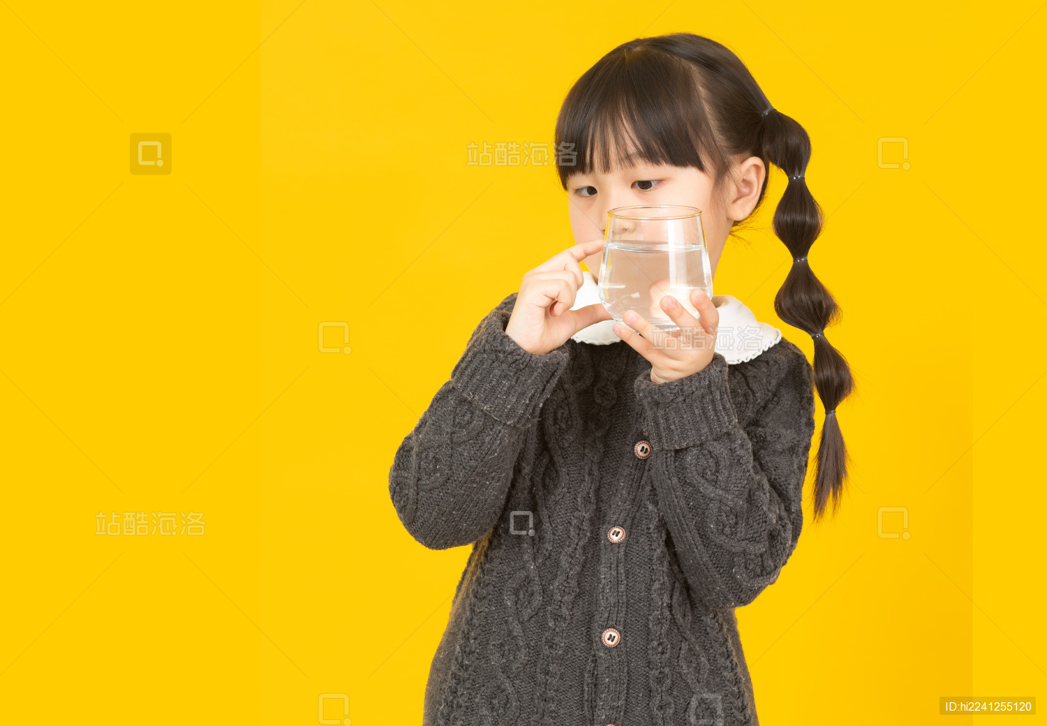 暖黄色背景前拿玻璃杯喝水的中国小女孩