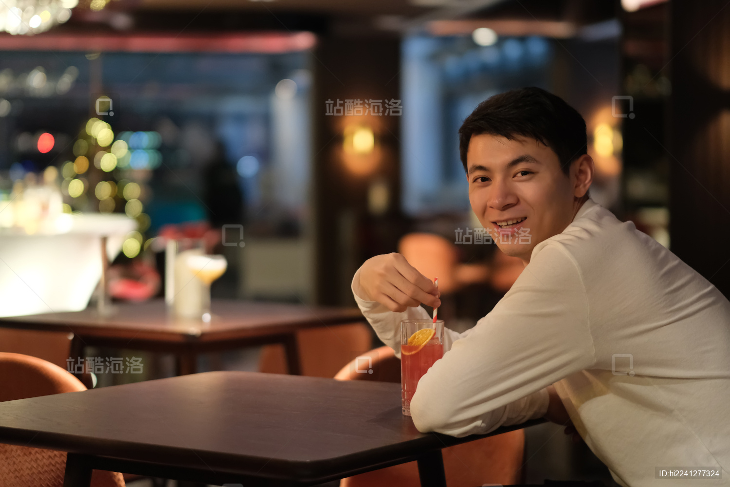 年轻的中国男子坐在夜晚的酒吧笑着喝鸡尾酒
