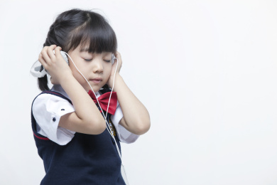 白背景前拿耳机听音乐的小学生
