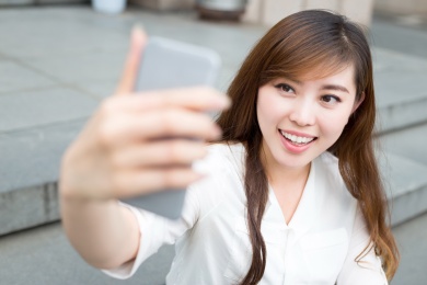 亚洲美丽的年轻女子用手机自拍采取户外。
