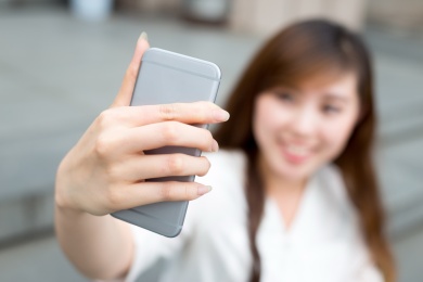 亚洲美丽的年轻女子用手机自拍采取户外。
