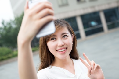 亚洲美丽的年轻女子用手机自拍采取户外。