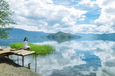 年轻女性坐在岸边废弃的木制平台上看镜头微笑 云南丽江大落水村