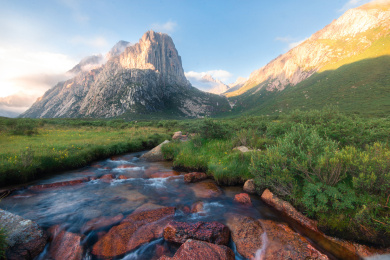 清晨的阳光照耀在山体上，映得金黄，让人感到十分温暖，小河从山间流下，冲击着河里的红色石头