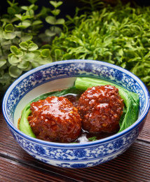 两颗红烧狮子头盛放在蓝边瓷碗里面