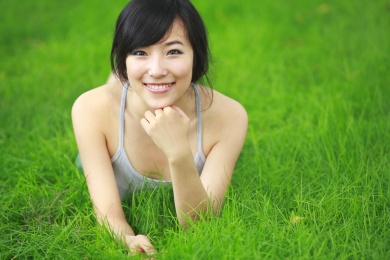 年轻漂亮的中国女子躺在相机绿色的草原微笑