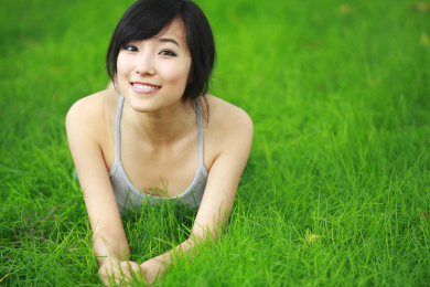 年轻漂亮的中国女子躺在相机绿色的草原微笑