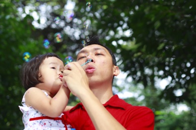 亚洲小女孩玩泡沫与她的父亲户外的