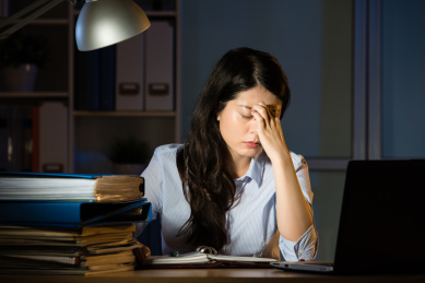 亚裔女商人坐在办公桌头痛加班深夜。在室内办公背景