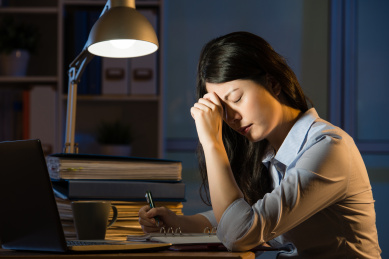 亚裔女商人坐在办公桌头痛加班深夜。在室内办公背景