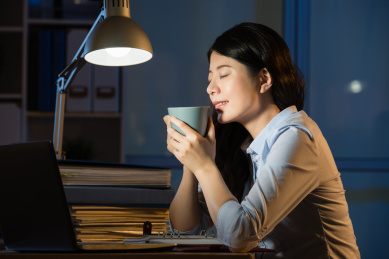 亚裔女商人喝咖啡提神加班深夜。在室内办公背景