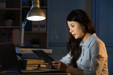 数字平板亚裔女商人触摸屏加班深夜。在室内办公背景