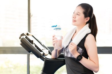 美丽的亚洲女子中休息拿着一瓶水跑跑步机后。室内健身房背景。健康运动理念