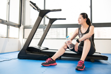 运动女人拿跑步机上使用智能手表饮水休息。室内健身房背景。健康运动理念