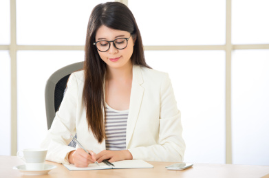 亚洲青年商人面带微笑,在办公室伏案写作