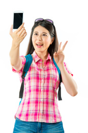 愉快亚洲女游客回吐自拍，胜利的手势在白色背景