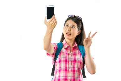 愉快亚洲女游客回吐自拍，胜利的手势在白色背景