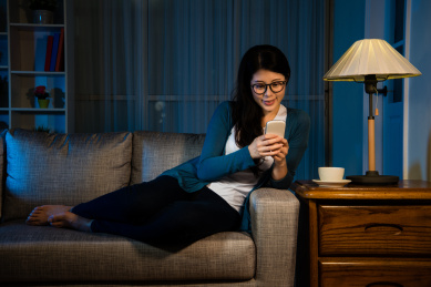 女子刚做完工作用的手机联系朋友在家里客厅坐在沙发上的时候,晚上