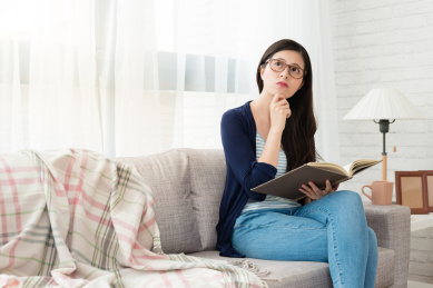 美丽的亚洲女性学生的阅读和思考在秋冬季节坐在家里客厅的沙发上