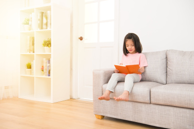 亚洲可爱的小女孩坐在客厅里一个人阅读有趣的漫画故事书在享受假日的早晨的阳光休闲时光感到快乐的沙发上。