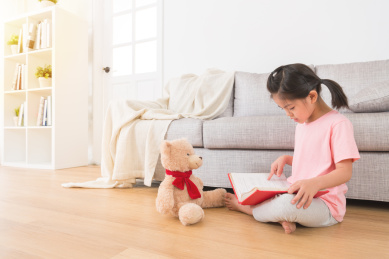 漂亮的姑娘儿告诉泰迪熊有趣的事情与指向的漫画故事书上的内容客厅很难在暑假学习的木地板坐在一起。