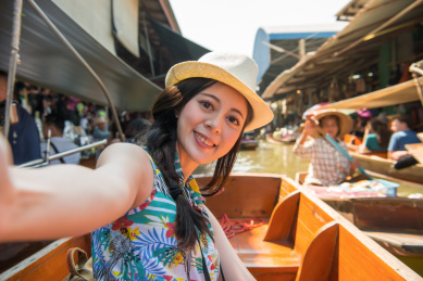 快乐漂亮的姑娘旅游服用自拍照片自拍的小船时，她亚洲泰国旅游期间访问流行的悬浮式市场。