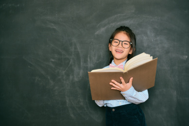 幸福甜蜜的小英语老师学校上课期间使用研究的书教的学生在黑板背景站立。