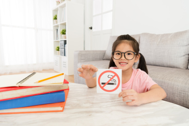 微笑可爱的小女孩在看相机呈现不吸烟的通知。