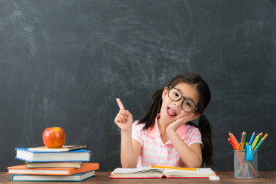 快乐有吸引力的小女孩面对镜头指向具有当她回到学校黑板在背景研究好主意空气。