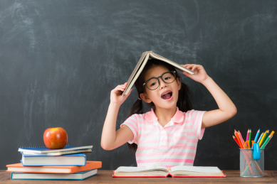 年轻快乐的女童重返学校就读坐在黑板背景，并把课本上的头看着相机。