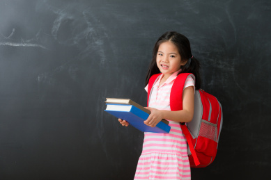 不快乐可爱的小女孩拿着学生课本重面对镜头的表现痛苦的情绪和黑板背景站在准备回学校学习。