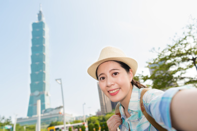 年轻的女背包客的亚洲正在台北最高建筑自拍。她满意台北市的景象。
