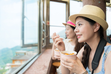 快乐的两个亚洲女性游客享受有当地著名的食品芋圆台北市的九份，望着从山顶伟大的海景。