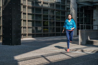 女运动员在美丽的夕阳现代建筑大楼附近独自跑来。健身慢跑锻炼健康概念。