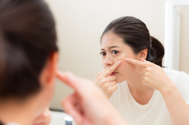年轻甜美的女人保持面部护理发现不健康的问题，当看着浴室镜子反射图像和手触摸脸颊挤痘痘。