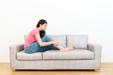 美丽优雅的女学生坐在沙发上沙发在木地板上看着她的腿时，她感觉发痒，使用手与白色背景划伤。