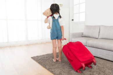 后视图吸引力的可爱女童牵着爱人玩具的照片熊站在客厅和携带行李箱准备一同前往。