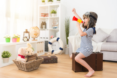 美丽漂亮的女小孩儿打扮成飞行员在游戏室坐在复古行李箱，并使用扩音器高喊宣布准备去冒险。