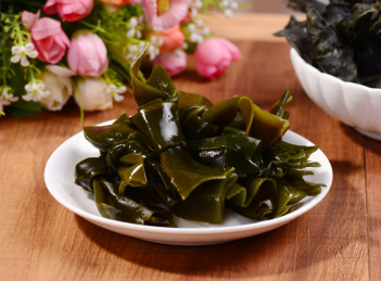 木桌背景下白色瓷盘中的海带结