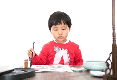 白背景里的书桌前认真写毛笔字的小女孩