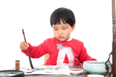 白背景里的书桌前认真写毛笔字的小女孩