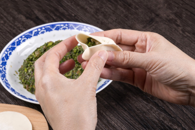 深色桌面摆放着水饺食材，双手正在包饺子