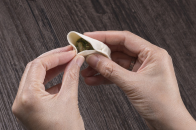 深色桌面摆放着水饺食材，双手正在包饺子