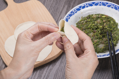 深色桌面摆放着水饺食材，双手正在包饺子