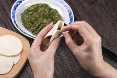 深色桌面摆放着水饺食材，双手正在包饺子
